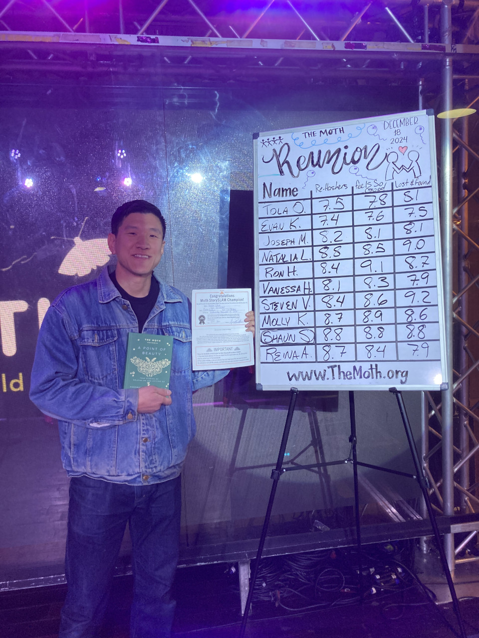 Me standing on a stage with a certificate and book, next to a scoreboard with my name circled with the highest score